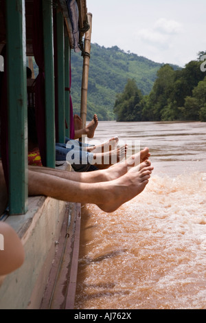 Passeggeri appendere i loro piedi dalle finestre sulla barca lenta tra Luang Prabang e Huay Xai sul fiume Mekong nella Loa Foto Stock