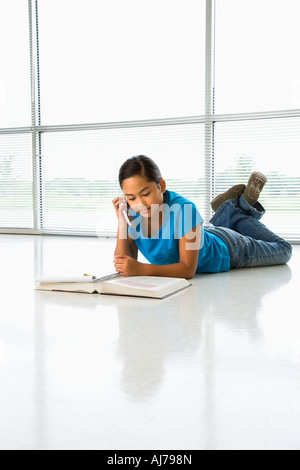 Asian preteen ragazza distesa sul pavimento facendo i compiti di scuola mentre parlano al telefono cellulare Foto Stock