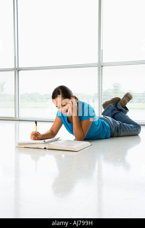 Asian preteen ragazza distesa sul pavimento facendo i compiti di scuola mentre parlano al telefono cellulare Foto Stock