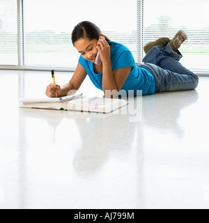 Asian preteen ragazza distesa sul pavimento facendo i compiti di scuola mentre parlano al telefono cellulare Foto Stock