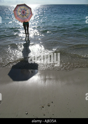 Donna che cammina dietro striata ombrello / ombrellone lungo la spiaggia, Maurizio Foto Stock