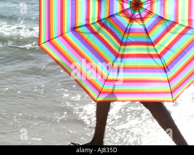 Donna che cammina dietro striata ombrello / ombrellone lungo la spiaggia, Maurizio Foto Stock