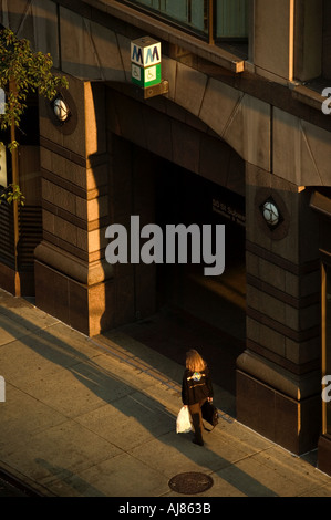 Donna cammina sul marciapiede in mattina presto luce di sole vicino alla stazione metropolitana fermata metropolitana sulla 48th Street in Midtown Manhattan New York NY Foto Stock