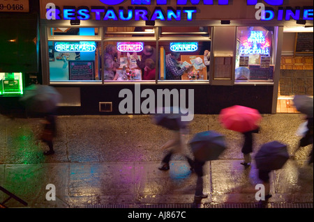 Persone con ombrelloni sulla notte piovosa passata a piedi tutta la notte cena sulla Ottava Avenue at 48th Street nel centro di Manhattan a New York Foto Stock