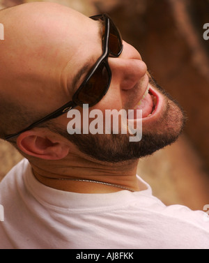 Uomo calvo con la barba indossando occhiali da sole guardando sopra la sua spalla. Foto Stock
