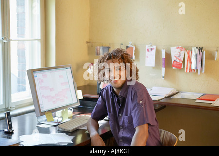 Giovane uomo sorridente dal computer in ufficio Foto Stock