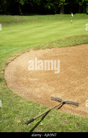 Primo piano di un rastrello in un bunker di golf con il verde in background Foto Stock