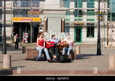 Le tre ragazze suonare la chitarra e cantare sotto una statua, Riga, Lettonia, UE Foto Stock