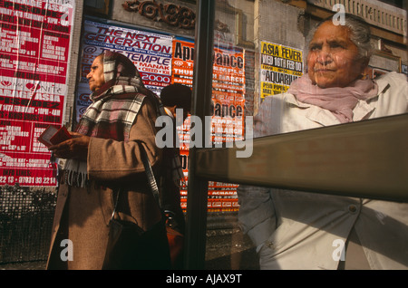 Anziani British Asian ladies attendere il loro autobus nei pressi di nuovo anno s notte manifesti pubblicitari dicendo Nuova Generazione Southall Foto Stock