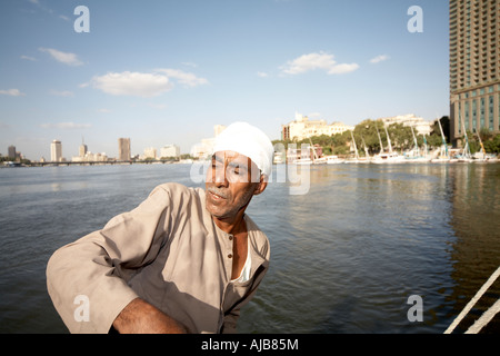 Barca egizia uomo nella tradizionale tunica galibeya sterzo feluca e barca a vela sul Fiume Nilo con Four Seasons Hotel Cairo Egitto Foto Stock