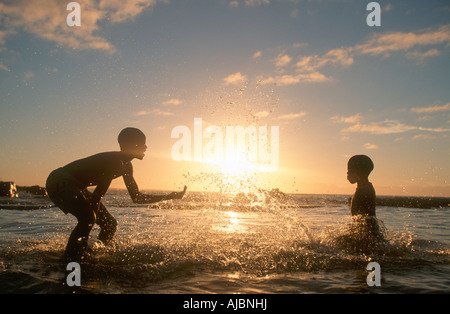 Due ragazzi giocare nel surf, stagliano al crepuscolo Foto Stock
