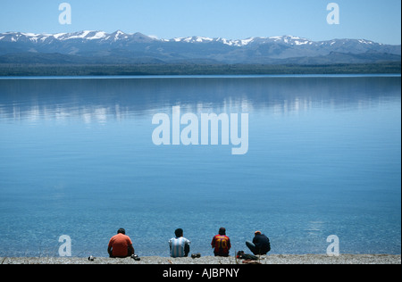 Quattro uomini seduti sul bordo di un lago con le montagne Snow-Capped in background Foto Stock