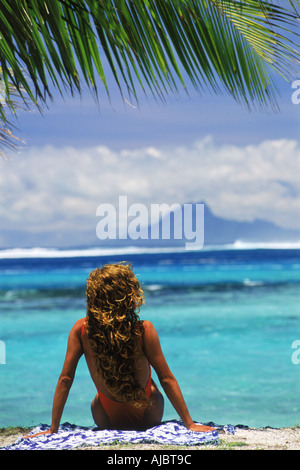 Donna seduta su Huahine Island Beach con Raitea isola al di là in Polinesia francese Foto Stock