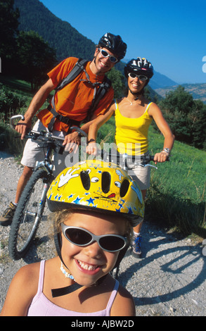 La famiglia in bicicletta nel paesaggio alpino, bambino indossando giallo ciclismo casco e occhiali da sole, i genitori vestita di nero ciclismo caschi un Foto Stock