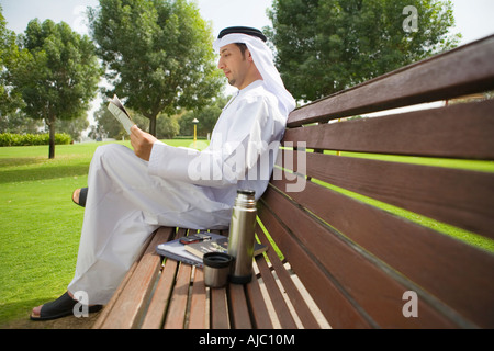 Uomo arabo quotidiano di lettura su una panchina nel parco Foto Stock