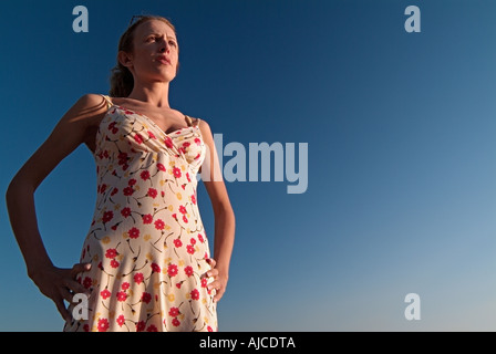 Giovane donna contro un cielo blu con le sue mani sui fianchi guardando fuori nel Big Blue Yonder sparato da un angolo basso vita fino Foto Stock