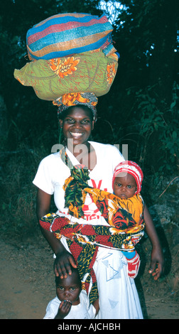Una giovane donna del Malawi che porta un grande cestino e il pacchetto sul suo capo e un bambino legato in un panno sulla sua spalla Foto Stock