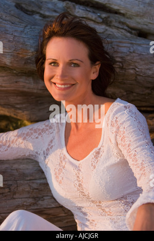 Donna in spiaggia ritratto da un log al tramonto Foto Stock