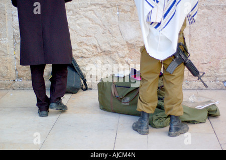 Due uomini ebrei pregare a Gerusalemme il Muro Occidentale- uno in tradizionale abito religioso, gli altri in uniforme militare con una mitragliatrice Foto Stock