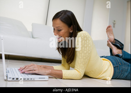 Donna sdraiata sul pavimento del salotto utilizzando laptop, vista terra Foto Stock