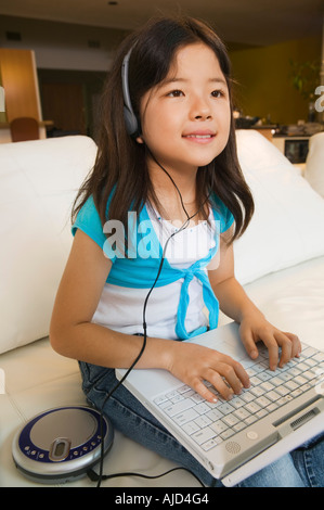 Ragazza seduta sul divano utilizzando laptop e ascolto di musica Foto Stock