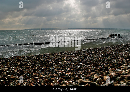 Acqua di Southampton, groyne in legno e la spiaggia di ciottoli insieme contro un imponente cielo a Calshot Spit, Calshot, Hampshire Foto Stock