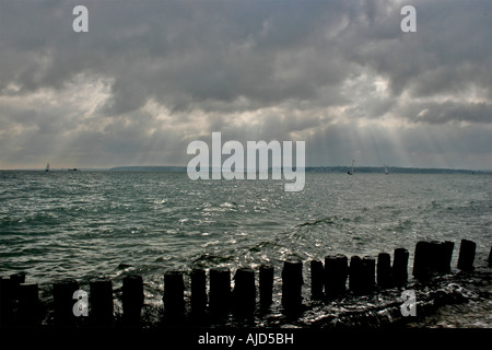 Acqua di Southampton, groyne in legno e la spiaggia di ciottoli insieme contro un imponente cielo a Calshot Spit, Calshot, Hampshire Foto Stock