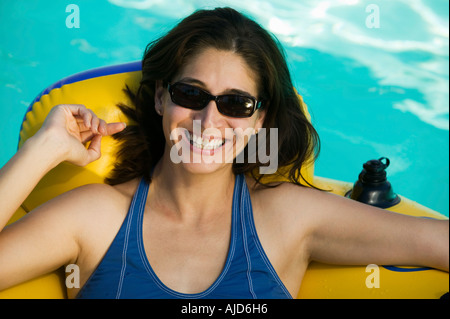 Donna che indossa gli occhiali da sole, giacente su zattera gonfiabile in piscina, ritratto. Foto Stock
