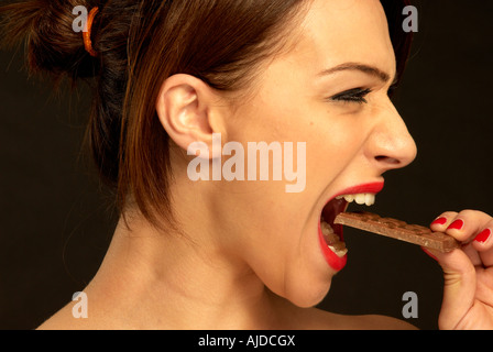 Donna di mordere in una barretta di cioccolato Foto Stock