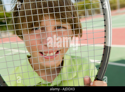 Ragazzo che guarda attraverso la racchetta da tennis, ritratto, close up Foto Stock