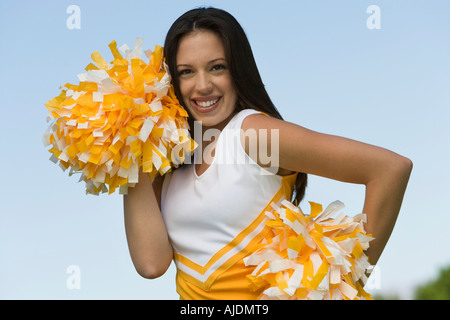 Sorridente Cheerleader holding pom-pom, (verticale). Foto Stock