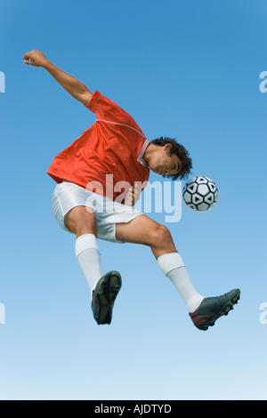 Giocatore di calcio saltando di testa la sfera nella metà di aria con cielo blu sullo sfondo Foto Stock