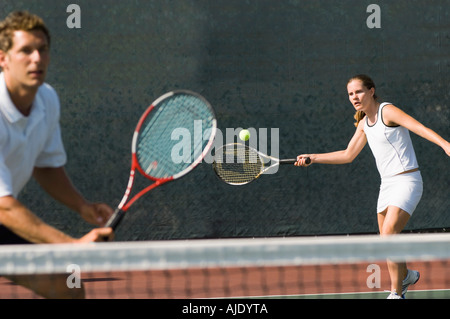 Doppio misto player colpendo palla da tennis, partner in piedi vicino al netto Foto Stock