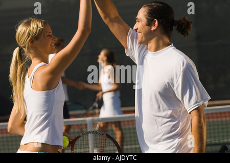 Doppio misto Partner High-Fiving ogni altro sul campo da tennis, vista laterale Foto Stock