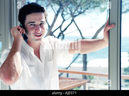 Giovane uomo su telefono cellulare vicino a finestra Foto Stock