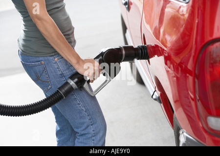 Giovane donna riempimento auto con gas, metà sezione Foto Stock