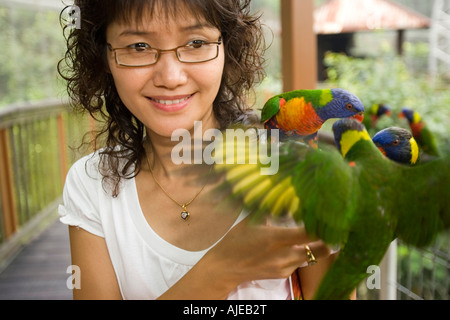 Giovane donna alimenta battibecco parrocchetti sul braccio del Jurong Bird Park Singapore Foto Stock