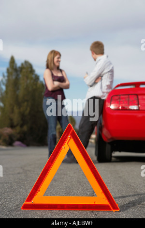 Due gli automobilisti in piedi da ripartiti in auto con un triangolo di avvertimento dietro di essa Foto Stock