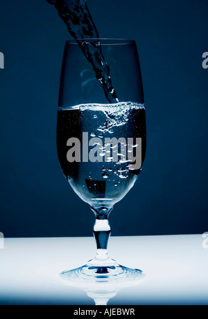 L'acqua versata in un bicchiere sguazzare accesa da sotto la creazione di un blu e freddo sentire alto contrasto Foto Stock