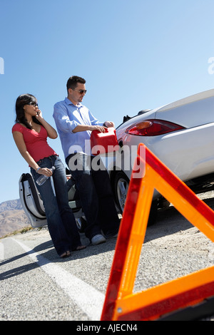 Il triangolo di avvertenza nella parte anteriore del giovane versando carburante in auto sulla strada del deserto Foto Stock