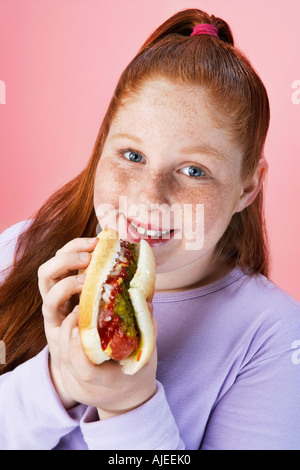 Il sovrappeso ragazza (13-15) mangiare hot dog, ritratto, close-up Foto Stock