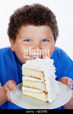 Il sovrappeso ragazzo (13-15) azienda grande fetta di torta, sorridente, ritratto Foto Stock