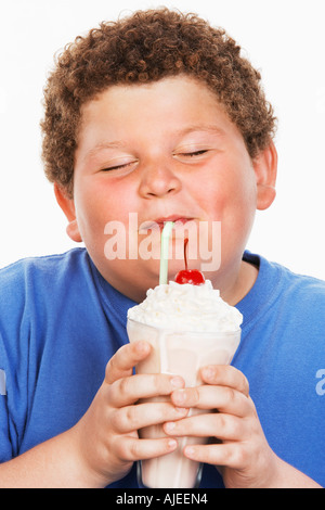 Il sovrappeso boy (13-15) bere latte shake, gli occhi chiusi, vista frontale Foto Stock