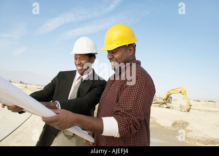 Lavoratori edili Indossare copricapi rigidi, guardando il piano sul sito Foto Stock