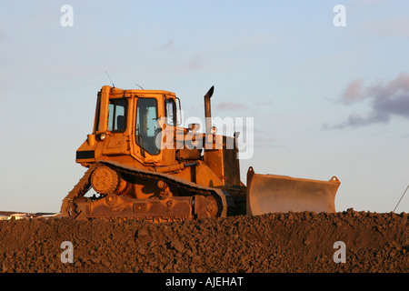 Un grande bulldozer giallo in piedi su una cresta contro il cielo Foto Stock