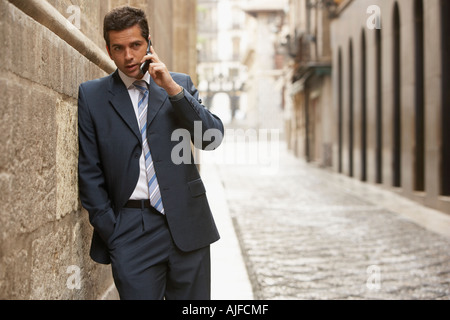 Imprenditore appoggiato su edificio in street, parlando al telefono cellulare. Foto Stock