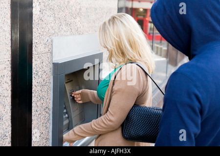 Ladro guardando sopra la spalla di donna al bancomat Foto Stock