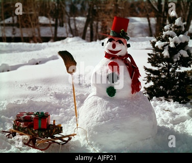 Pupazzo di neve tenendo una scopa con slitta impilati con allegramente avvolto di Natale pacchetti vacanza Foto Stock