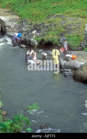 Tre donne di Maurizio a lavare i panni in un fiume mentre un giovane ragazzo orologi, Flacq, Mauritius Foto Stock