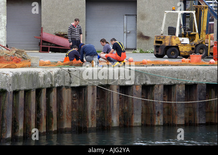 I pescatori riparare le loro reti da pesca sul lato della banchina di Kilkeel Harbour contea di Down Irlanda del Nord Foto Stock